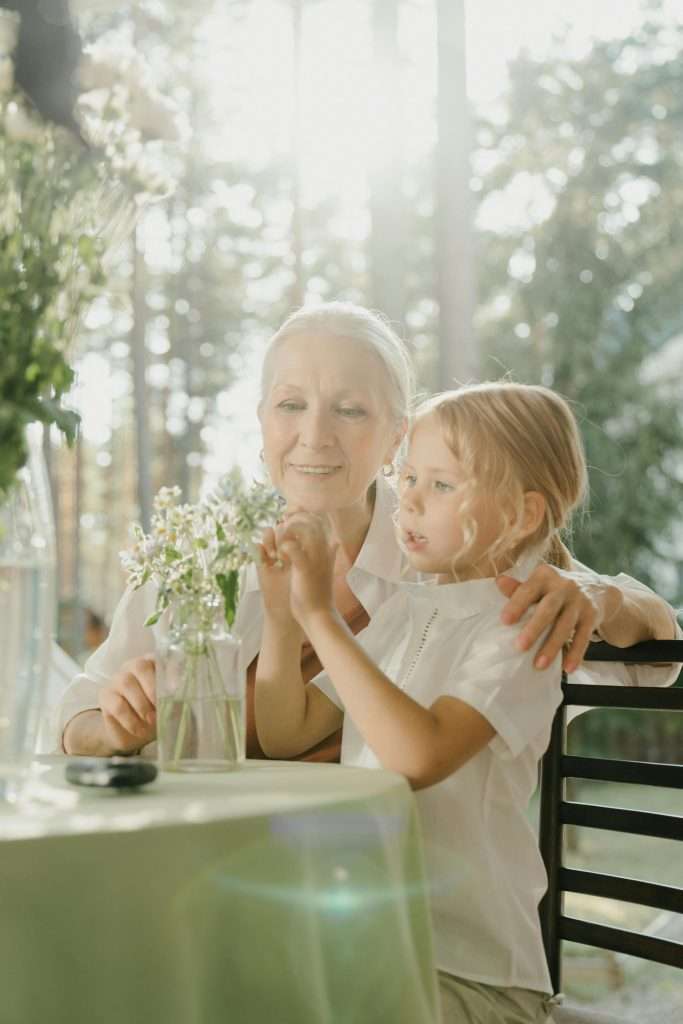 grandmother putting flowers in a vase with a young grandchild